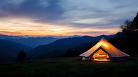 Illuminated glamping tent in mountain wilderness at sunset with dramatic sky and layered peaks creating peaceful outdoor adventure camping experience.