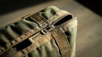 Military tactical backpack with camouflage pattern and zipper detail on wooden surface for outdoor adventure and combat gear applications.