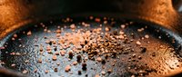 Close-up of ground coffee beans scattered on dark roasted surface with warm lighting, suitable for beverage, café, and food industry marketing materials.