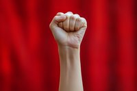 Raised fist against dramatic red background symbolizing power, protest, resistance and solidarity. Strong lighting emphasizes determination and strength.