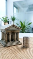 Miniature bank building model with coin stack on wooden desk in modern office interior for financial planning and investment concepts.