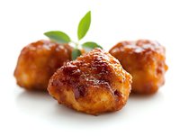 Glazed meatballs garnished with fresh green leaves on white background, close-up view showing juicy texture and caramelized coating. Appetizing party food.
