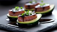 Fresh tuna slices on avocado halves drizzled with balsamic reduction and microgreens, served on black slate plate for gourmet appetizer presentation.