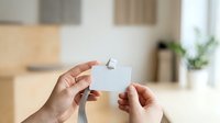Two people exchanging blank white business card in modern office environment with natural lighting and blurred interior background for corporate branding mockup.