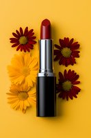 Red lipstick with burgundy and yellow daisies arranged on vibrant yellow background. Minimalist cosmetic flatlay composition for beauty and makeup advertising.