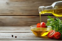 Pouring golden olive oil into glass bowl with fresh cherry tomatoes and herbs on rustic wooden background, Mediterranean cuisine ingredients.