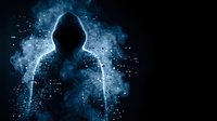 Mysterious hooded figure silhouette surrounded by glowing blue digital particles and smoke effects on dark background for cybersecurity concepts.