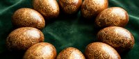 Golden ornate Easter eggs with intricate floral patterns arranged in circle on emerald green velvet fabric for holiday celebration and spring decoration.