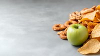 Fresh green apple with assorted salty snacks and nuts on gray concrete background with copy space for menu, recipe or healthy eating concept.