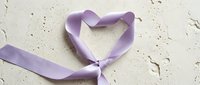 Purple satin ribbon twisted into heart shape on textured white background for romantic occasions, weddings, Valentine's Day celebrations and love concepts.