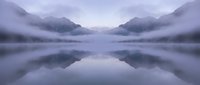 Serene mountain lake with perfect reflections in misty dawn light, purple and blue tones creating peaceful atmospheric landscape for meditation and wellness.