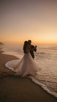 Romantic newlywed couple dancing on beach at sunset during golden hour wedding celebration with ocean waves and dramatic sky creating intimate moment.