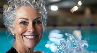 Active senior woman with gray curly hair and bright smile enjoying water aerobics in indoor pool, wellness and healthy lifestyle concept for elderly people.