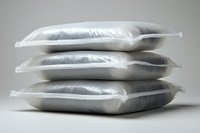 Stack of white soft pillows in transparent plastic packaging on light background, showing texture and volume of bedding accessories for home decor and comfort.
