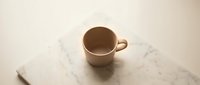 Empty beige ceramic coffee mug on white marble surface with natural lighting for kitchen and dining concepts.