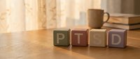 PTSD wooden blocks on desk with warm lighting, representing mental health awareness and psychological disorder education.