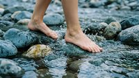 Bare feet walking on wet river rocks with flowing water, natural outdoor adventure and wellness concept for relaxation and mindfulness activities.