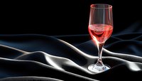 Glass of rose wine on black silk fabric with elegant folds creating dramatic lighting and shadows, luxury beverage photography against dark background.