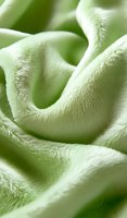 Soft mint green velvet fabric with gentle folds and curves creating abstract waves and shadows, macro photography showing detailed textile texture and plush surface.