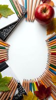 School supplies frame with colored pencils, notebooks, red apple and autumn leaves creating circular border on white background for education design.
