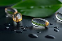 Water drops on dark surface with green leaf reflection creating natural lens effect, macro photography showing surface tension and environmental concept.