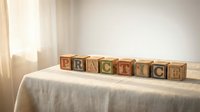 Wooden alphabet blocks spelling PRACTICE arranged on white fabric surface in bright natural light creating educational learning concept for children development.