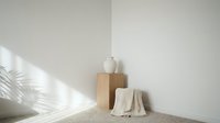 Minimalist corner interior with wooden stool and white ceramic vase casting natural palm leaf shadows on neutral beige wall for modern home decor.