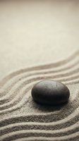 Zen meditation stone on raked sand garden creating peaceful mindfulness atmosphere for spa wellness and relaxation therapy concepts.