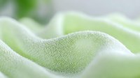 Soft green fabric texture with gentle folds and waves creates calming minimalist background pattern. Natural cotton or linen material in macro photography.