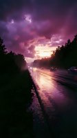 Wet highway at dusk with dramatic purple and pink storm clouds overhead, vehicles with headlights on wet asphalt, forested landscape, moody atmospheric weather conditions.