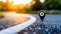 Location pin marker on curved asphalt road with sunset bokeh background, shallow depth of field focus on navigation symbol for travel and journey concept.
