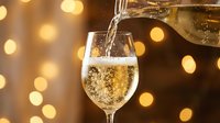Champagne pouring into glass with golden bokeh lights in background, celebration and festive occasion for holidays, parties, weddings and toasts.