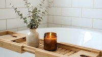 Wooden bath tray with eucalyptus plant in ceramic vase and amber glass candle on white subway tile background for spa and home decor.