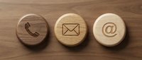 Wooden contact buttons with phone, email, and at symbol icons on natural wood surface for business communication.