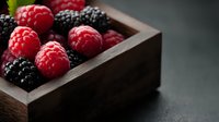 Fresh ripe raspberries and blackberries in rustic wooden box on dark background, macro food photography with selective focus and copy space.