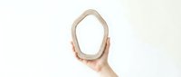 Hand holding wooden oval mirror frame against white background for interior design and home decor projects.