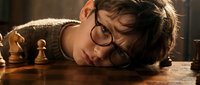 Young man with glasses resting head on wooden chess board during strategic game planning session in warm indoor lighting atmosphere.