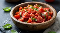 Fresh diced tomatoes with basil leaves in rustic wooden bowl on dark slate surface. Healthy Mediterranean ingredients for cooking and salads.