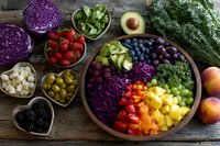 Fresh colorful fruits and vegetables arranged in bowls on wooden table, including berries, avocado, cabbage, peppers, and leafy greens for healthy eating.