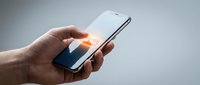Hand holding smartphone with glowing fingerprint scan on screen, biometric security authentication concept on gray background.
