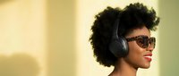 Young African American woman with curly afro hair wearing sunglasses and wireless headphones enjoying music with warm golden lighting for lifestyle content.