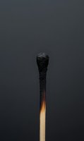 Burnt wooden matchstick with charred black head against dark gray background symbolizing burnout, exhaustion, failure or end of resources.