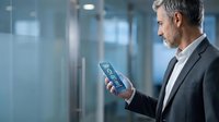 Mature Caucasian businessman in suit using smartphone in modern office environment with glass walls and professional lighting.