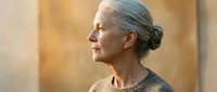 Senior woman with gray hair in bun wearing knit sweater looking thoughtfully to side in warm golden light for lifestyle and aging concepts.