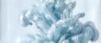 Blue ink dissolving in water, creating swirling cloud formations with glittering silver particles, soft abstract texture on light background.
