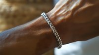 Close-up of elegant silver chain bracelet on male wrist with warm natural lighting showcasing luxury men's jewelry and sophisticated style accessories.