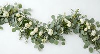 Elegant eucalyptus garland with white roses and delicate greenery for wedding decor, table centerpiece, or special event styling on white background.
