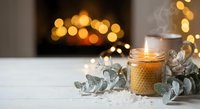 Cozy winter evening scene with burning candle, eucalyptus leaves and warm bokeh lights creating peaceful holiday atmosphere for home decor and relaxation.