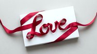 Elegant white gift card wrapped with a red satin ribbon forming the word Love, perfect for Valentine's Day and romantic occasions.