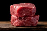 Fresh raw beef tenderloin steaks stacked on rustic wooden surface against dark background. Premium cut meat showing marbling and texture for cooking.